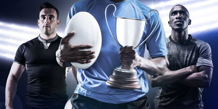Mid section of sportsman holding trophy and rugby ball against spotlights