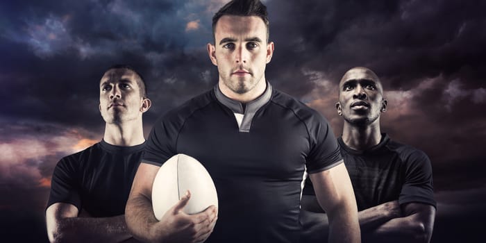 Tough rugby player holding ball against blue and orange sky with clouds