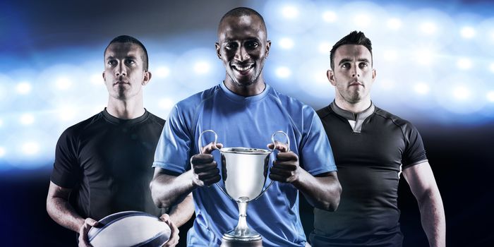 Portrait of happy athlete holding trophy against spotlights