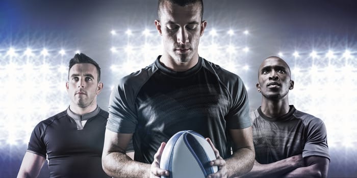 Thoughtful rugby player holding ball against spotlight
