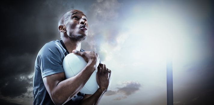 Rugby player catching ball while playing against spotlight in sky