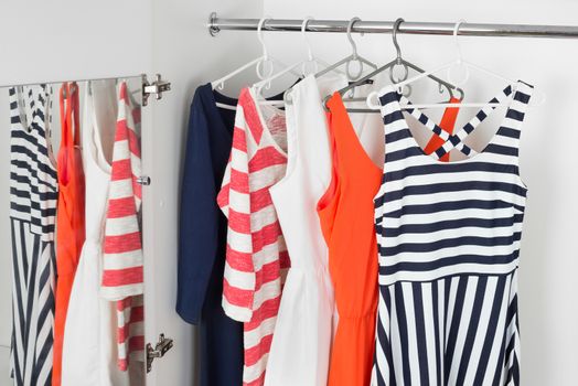 a series of bright modern fashion women's dresses on hangers in a white cupboard for summer and spring