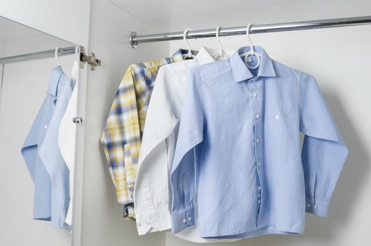 white blue and checwhite  blue and checkered clean ironed men shirts hanging on hangers in the white wardrobe