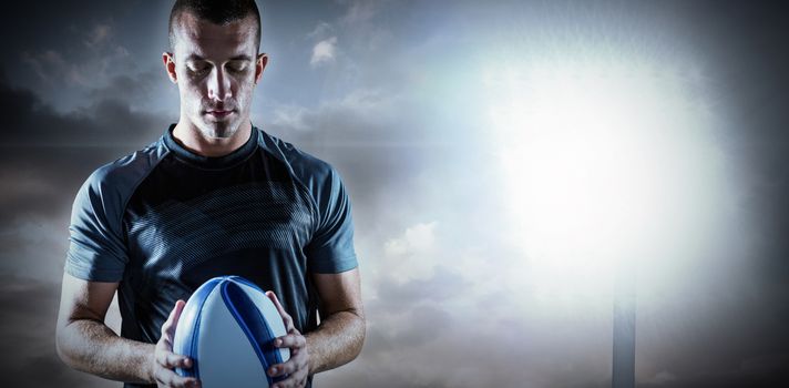 Thoughtful rugby player holding ball against spotlight in sky