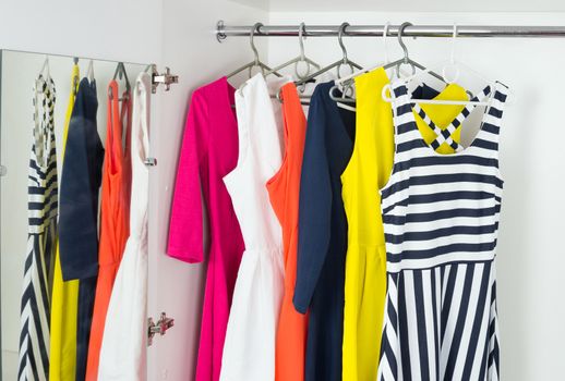 a series of bright modern fashion women's dresses on hangers in a white cupboard for summer and spring