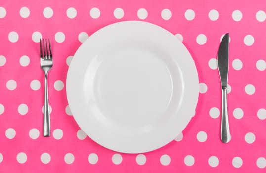 White ceramic plate, metal fork and knife on the table, a bright pink tablecloth with white polka dots. Concept of food choice, diet, weight loss, lifestyle. Breakfast, lunch, dinner.