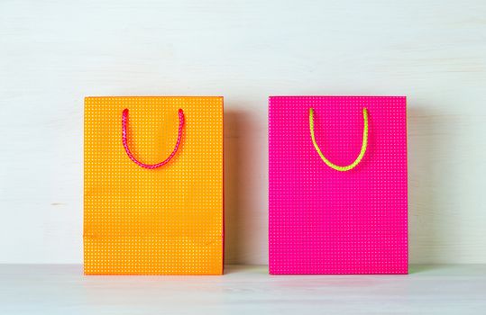 Two bright multicolored shopping bags on a white wooden background