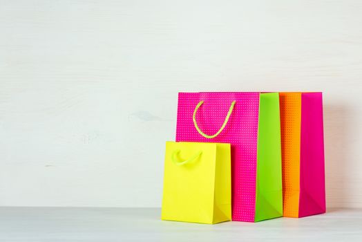 Three bright multi-colored shopping bags on a white wooden background