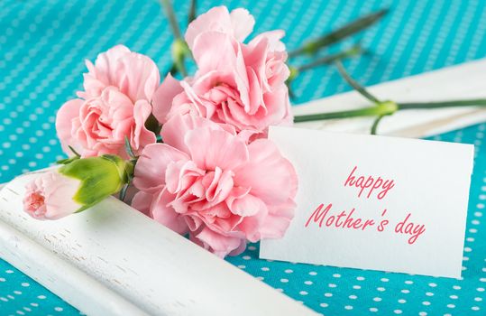 Greeting card with the inscription Happy Mothers Day with pink carnations on a bright blue background with white polka dots