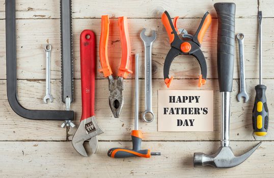 Greeting Card to Happy Father's Day, concept, set of different tools: a hammer, Hand saw, pliers, wrench, screwdriver, various spanners, clamp on a wooden background and text , closeup, top view