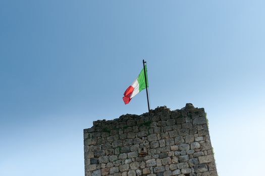 Italian flag backlit by sun above historic stone wall.