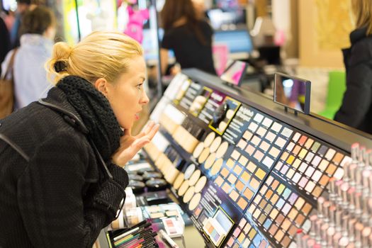 Beautiful blond lady testing  and buying cosmetics in a beauty store.