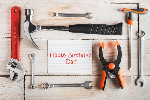 Greeting Card to Happy Birthday Dad, concept, set of different tools: a hammer, wrench, screwdriver, various spanners, clamp on a wooden background and tablet with text Happy Birthday Dad 