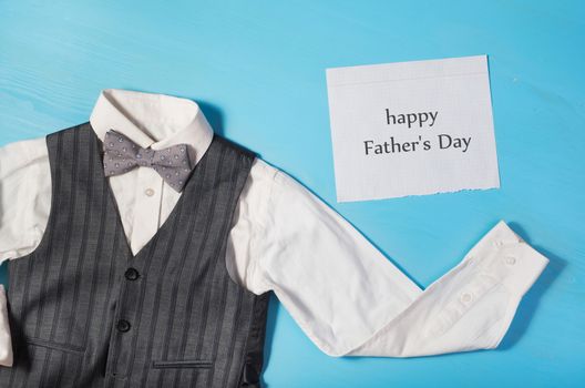 white shirt, gray vest and a bow tie and a sheet of paper with text  happy Father's Day on a bright blue background