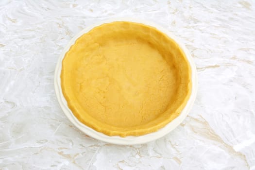 Circular ceramic pie dish lined with homemade pastry on a kitchen work surface