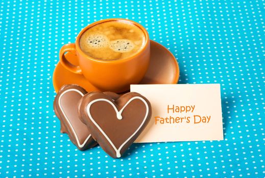ceramic cup with coffee  espresso, tablet with text Happy Father's Day and two chocolate marzipan candy hearts on a bright blue background, love concept