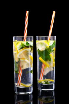 Water with lemon and mint. Cold refreshing, natural, organic, healthy drinks. Two glasses of lemonade with cocktail straws. Isolated on black background