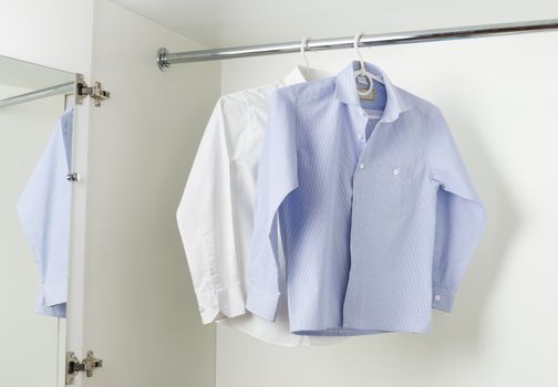 white and blue clean ironed men's shirts hanging on hangers in the wardrobe white