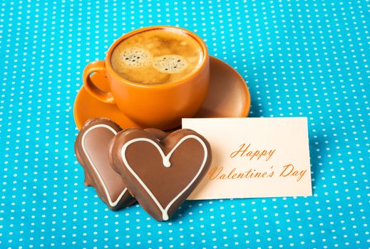 ceramic cup with coffee  espresso, tablet with text  happy Valentine's Day and two chocolate marzipan candy hearts on a bright blue background, love concept