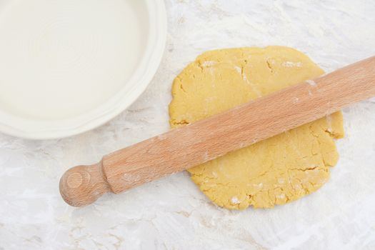 Rolling out homemade pastry with a wooden rolling pin next to a ceramic pie dish