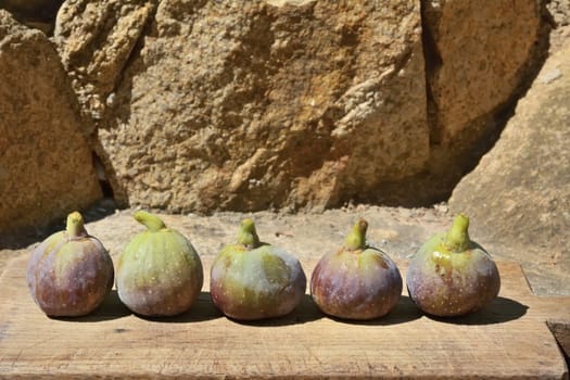 Composition of fig fruits on a wooden board and rocks in the background. 