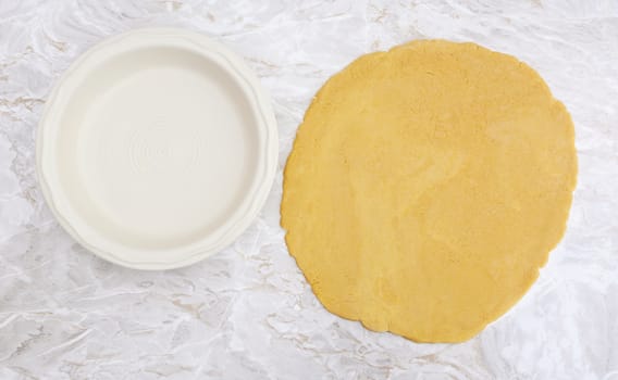 Fresh shortcrust pastry rolled out in a circle, ready to line ceramic pie dish
