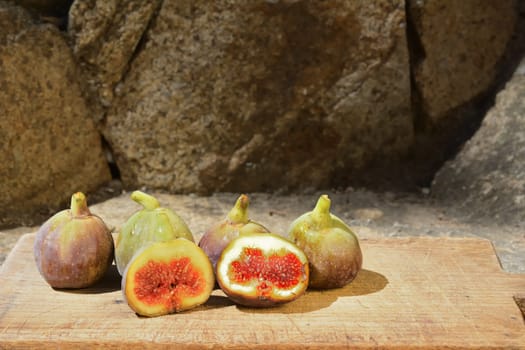 Composition of fig fruits on a wooden board and rocks in the background.