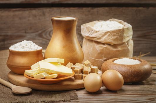 Baking ingredients, flour, butter, milk, sugar and eggs in a rustic style on the old wooden background