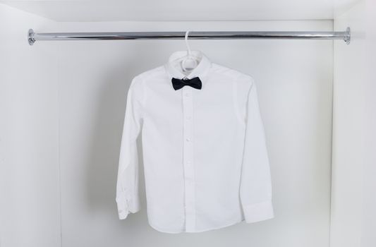 white  men's shirt with black bow tie hanging on hangers in the closet white