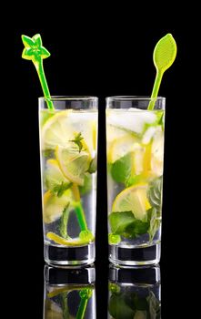 Water with lemon and mint. Cold refreshing, natural, organic, healthy drinks. Two glasses of lemonade with Cocktail Sticks. Isolated on black background