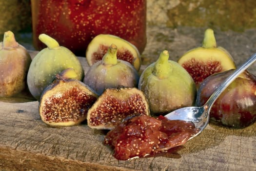 Composition of fig fruits on a wooden board and rocks in the background. Marmalade in the background over a spoon.