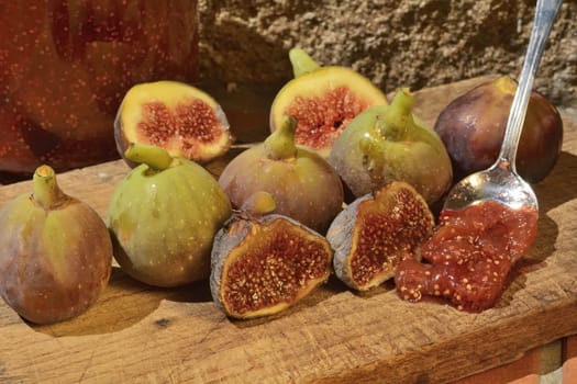 Composition of fig fruits on a wooden board and rocks in the background. Marmalade in the background over a spoon.
