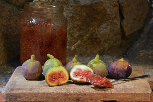 Composition of fig fruits on a wooden board and rocks in the background. Marmalade in the background over a spoon.