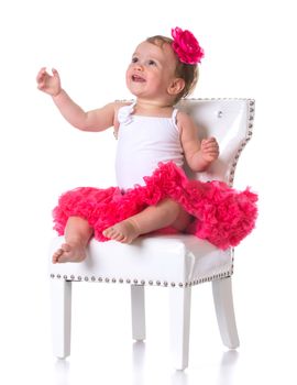 happy one year old girl wearing tutu sitting on a white chair