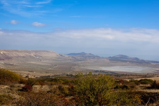 An autumn valley with bushes and blue sky
