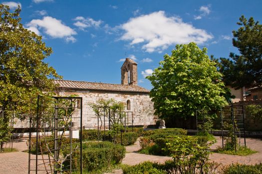 An old stone roman church and a garden in San Quirico d'Orcia in Italy

