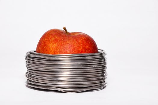 Wired apple: whole red apple in coils of aluminum wire isolated on white background