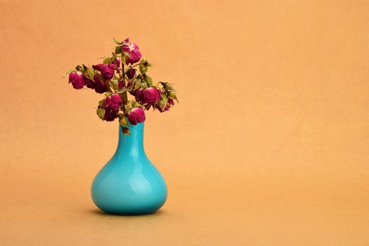 Dried-up red roses bouquet in a blue vase on background of kraft paper (landscape layout, left take)