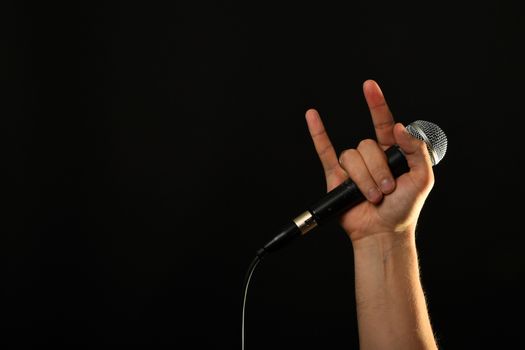 Male hand holding microphone with devil horns rock metal sign isolated on black background