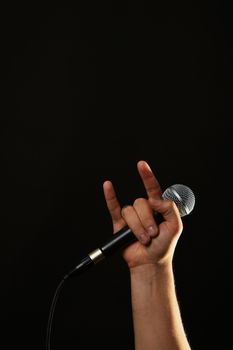 Male hand holding microphone with devil horns rock metal sign isolated on black background