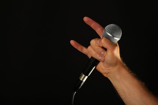 Male hand holding microphone with devil horns rock metal sign isolated on black background