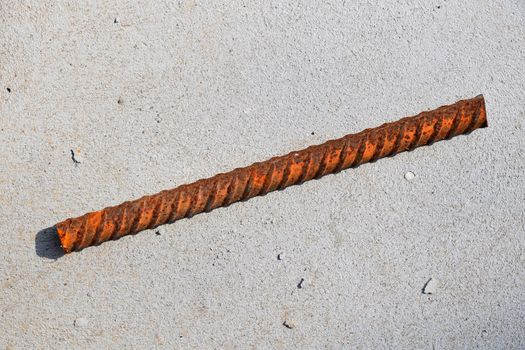 Cut piece of corroded stained rusty metal armature fitting on bubbled concrete floor