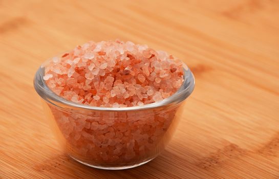 Himalayan pink salt in tiny transparent glass bowl on wooden bamboo background