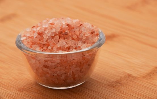 Himalayan pink salt in tiny transparent glass bowl on wooden bamboo background