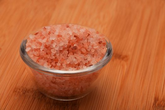 Himalayan pink salt in tiny transparent glass bowl on wooden bamboo background