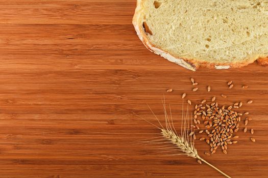 Wooden bamboo cutting board with one wheat ear, handful of ripe grains and a slice of bread - add your text
