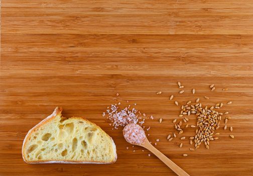 Wooden bamboo cutting board with spoon of pink Himalayan salt, handful of ripe grains and slice of bread - add your text