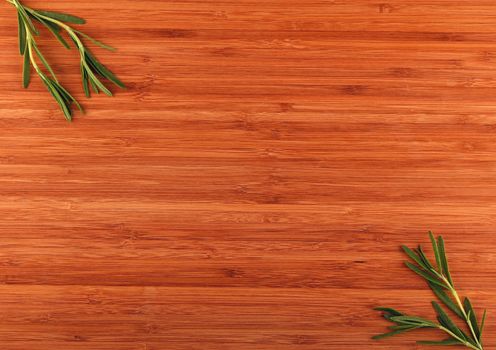Wooden bamboo cutting board with rosemary leaves in corners