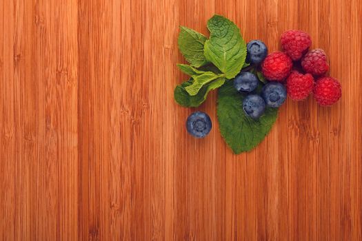 Taste of summer, cutting board with mellow blueberries, raspberries and mint leaves