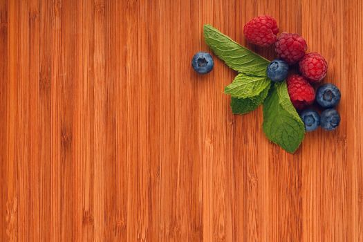 Taste of summer, cutting board with mellow blueberries, raspberries and mint leaves